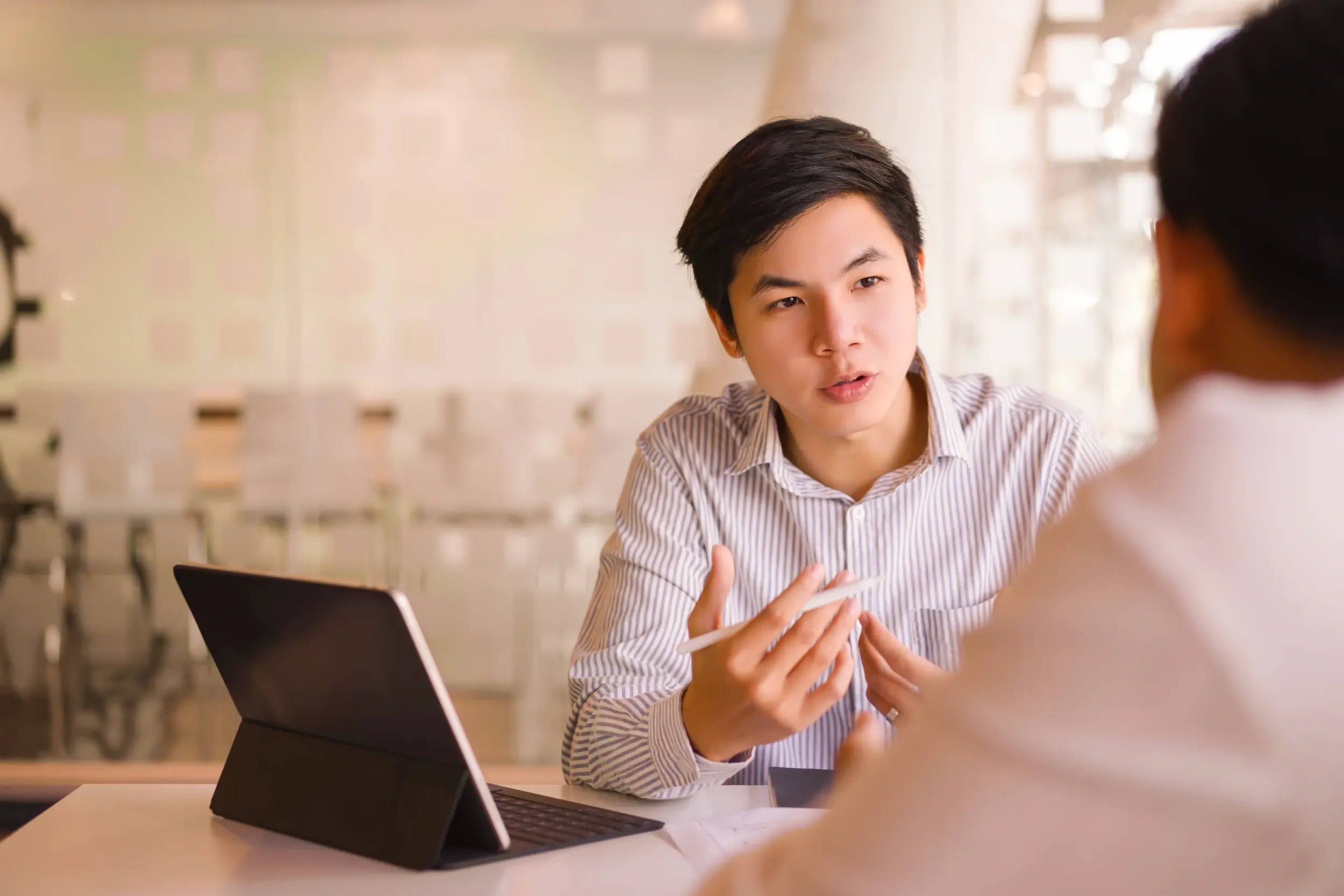 Man gesturing with a pen while explaining something across the table during a meeting.